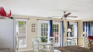 Une pièce comprenant une table à manger, des chaises, un ventilateur de plafond et une fenêtre avec des rideaux.