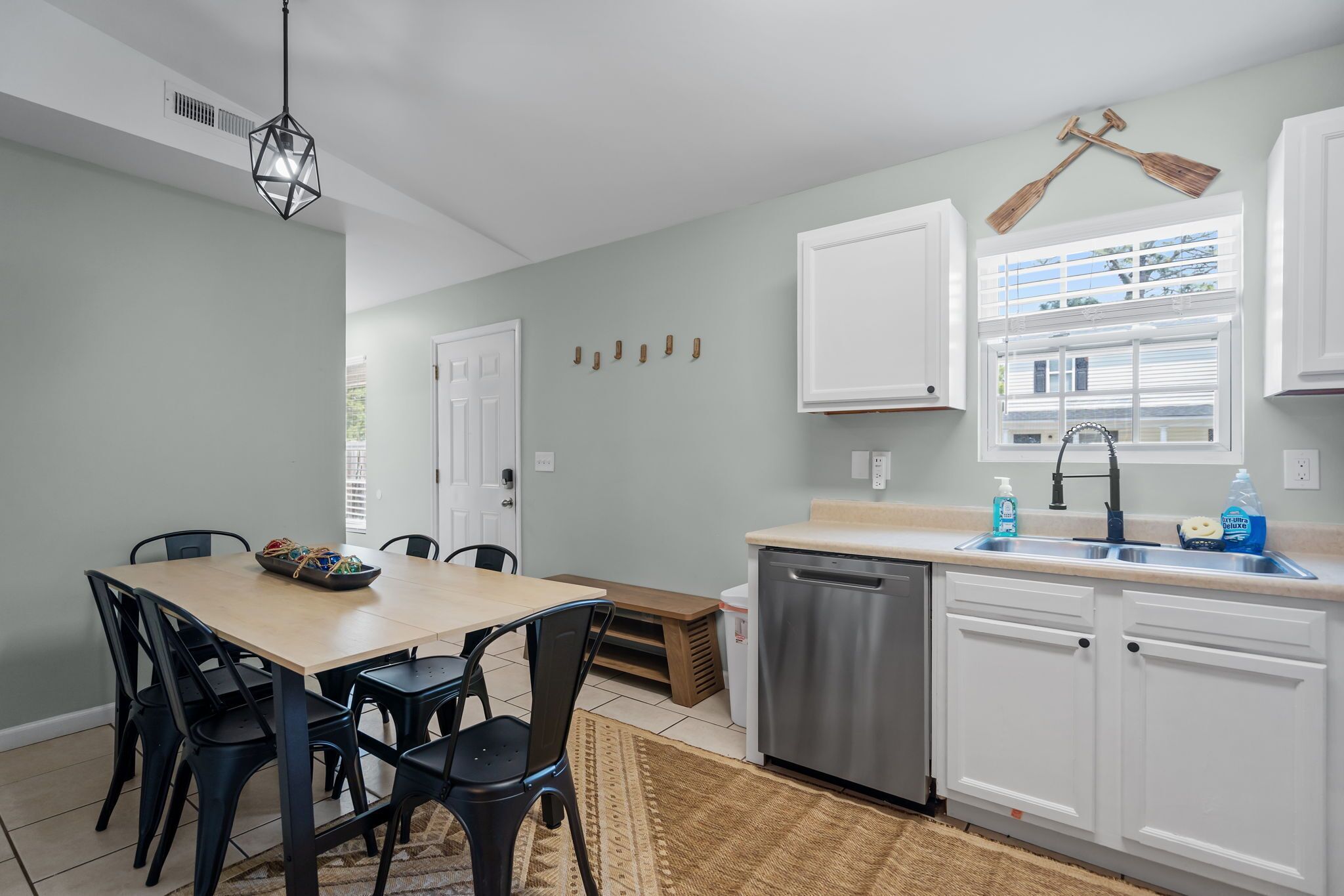 A kitchen with a dining table, chairs, a dishwasher, and a window with blinds.