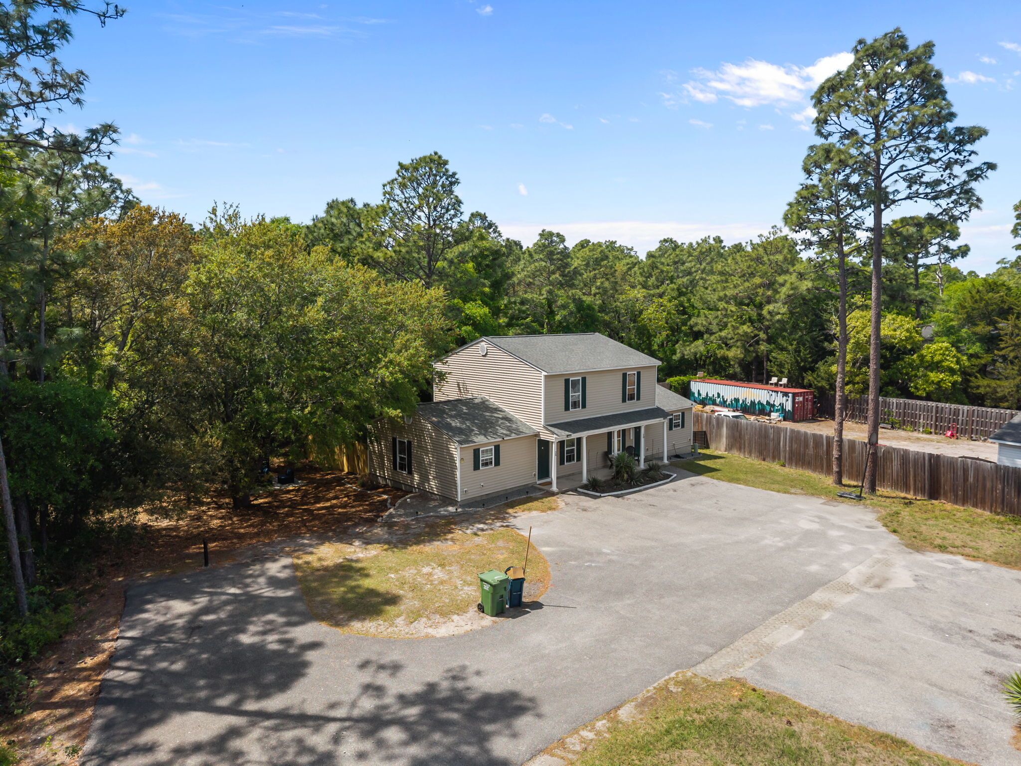 A two-story house with a front porch, surrounded by trees and a fenced yard.