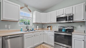 A modern kitchen with white cabinetry, stainless steel appliances, and a window with blinds. - Portside Retreat: Quiet wooded stay, where everything just short drive away (Wilmington)