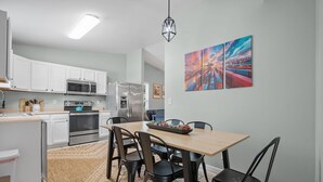 A modern kitchen with white cabinets, stainless steel appliances, and a dining area with a wooden table and chairs. - Portside Retreat: Quiet wooded stay, where everything just short drive away (Wilmington)