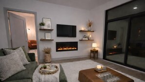Ein Wohnzimmer mit Sofa, Couchtisch, Kamin, Fernseher und Regalen mit Dekorationsgegenständen.