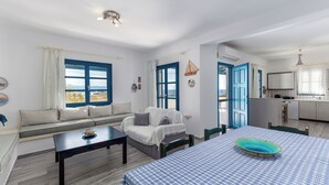 Een kamer met een bank, een eettafel, een keuken en uitzicht door een raam.