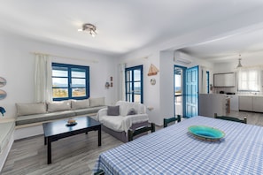 Ein Zimmer mit einer Couch, einem Esstisch, einer Küchenzeile und Blick durch ein Fenster.