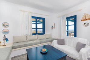 Ein Zimmer mit einer Couch, einem Couchtisch und Blick durch ein Fenster mit blauen Fensterläden.