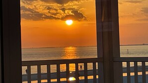 Zonsondergang te zien door een raam met balkon, uitkijkend over de zee.