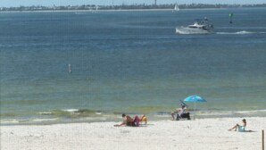 Een strand met een zandrijk strand, enkele mensen en een boot in het water.