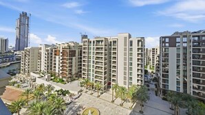 A modern residential building complex with multiple high-rise apartments, a central courtyard with palm trees, and a river in the background. - Work & Chill 1BR w/ Office + PS5 Dubai Creek (Dubai)