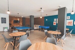 A room with a pool table, foosball table, and multiple seating areas with tables and chairs.