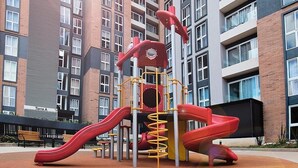 Een speeltuin met glijbanen en klimconstructies, omgeven door een gebouw met meerdere ramen en balkons.