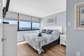 A bedroom with a bed, a nightstand, a window with a view, and a door. - Shore Drive 2 bedroom sleeps 4 Myrtle Beach (Myrtle Beach)