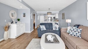 A modern living room with a sofa, coffee table, and a kitchen in the background. - Shore Drive 2 bedroom sleeps 4 Myrtle Beach (Myrtle Beach)