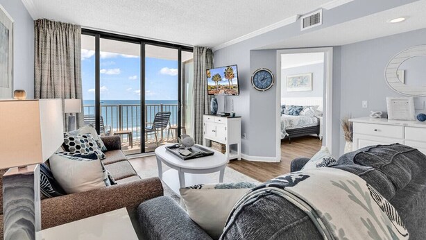 A modern living room with a sofa, a coffee table, and a TV. There is a balcony with a view of the sea. - Shore Drive 2 bedroom sleeps 4 Myrtle Beach (Myrtle Beach)