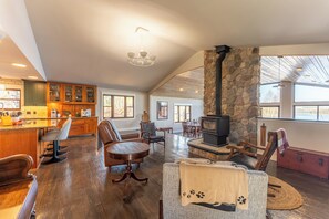 A spacious living area with a stone fireplace, wooden furniture, and a kitchen with green cabinets.
