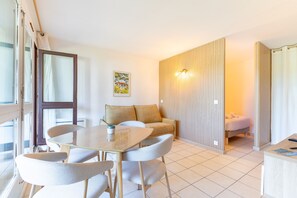A modern room with a glass table, white chairs, a sofa, a bed, and a wooden partition. - Little Pignada - Proche Plage (Seignosse)