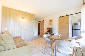 A modern living space with a sofa, a dining table with chairs, a TV, and a refrigerator. - Little Pignada - Proche Plage (Seignosse)