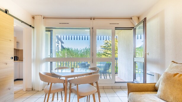 En moderne stue med en glasdør, der fører ud til en balkon, et rundt bord med stole og en sofa.