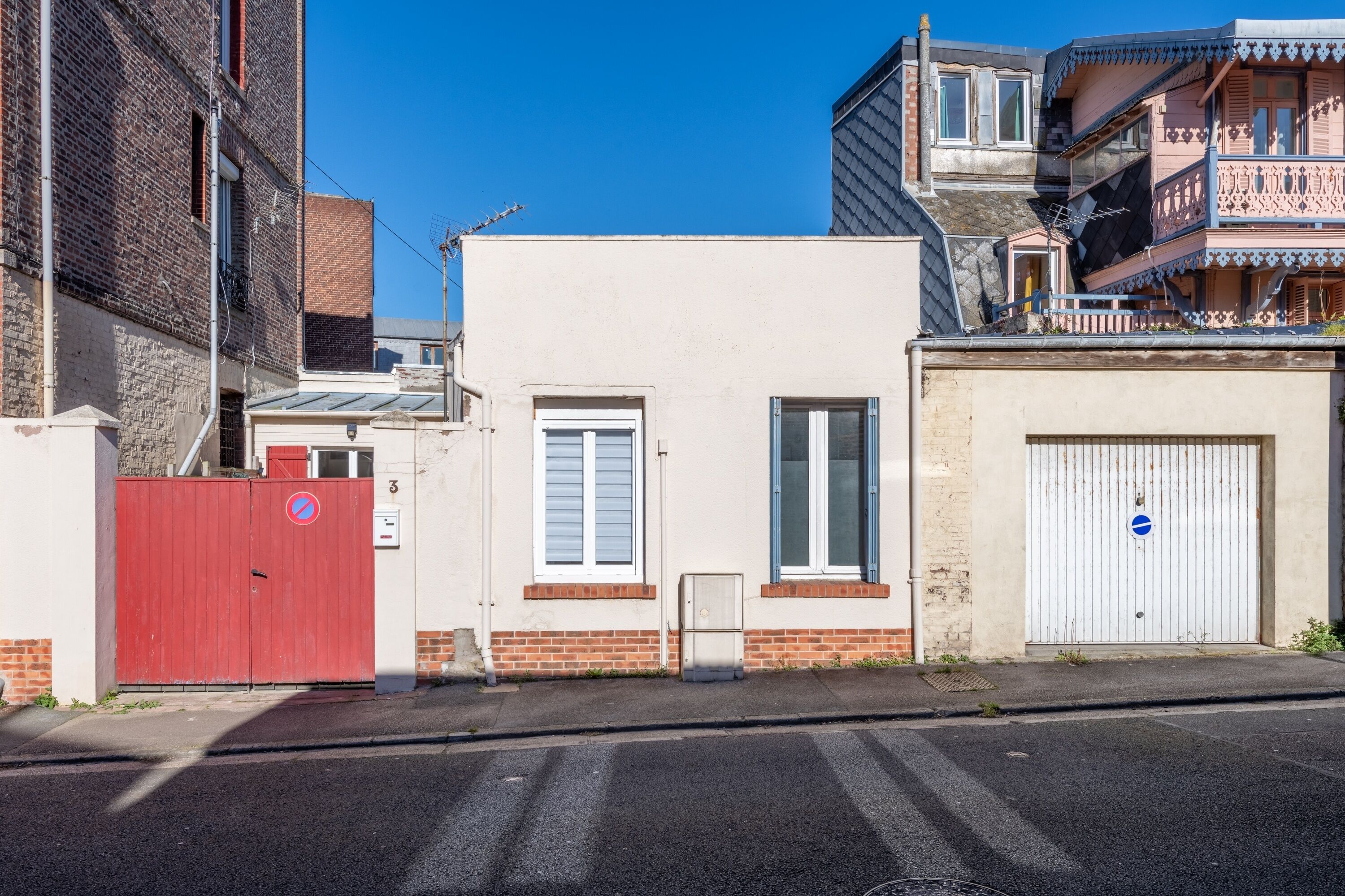 A narrow street with a red gate, a white building with a garage door, and a brick wall.
