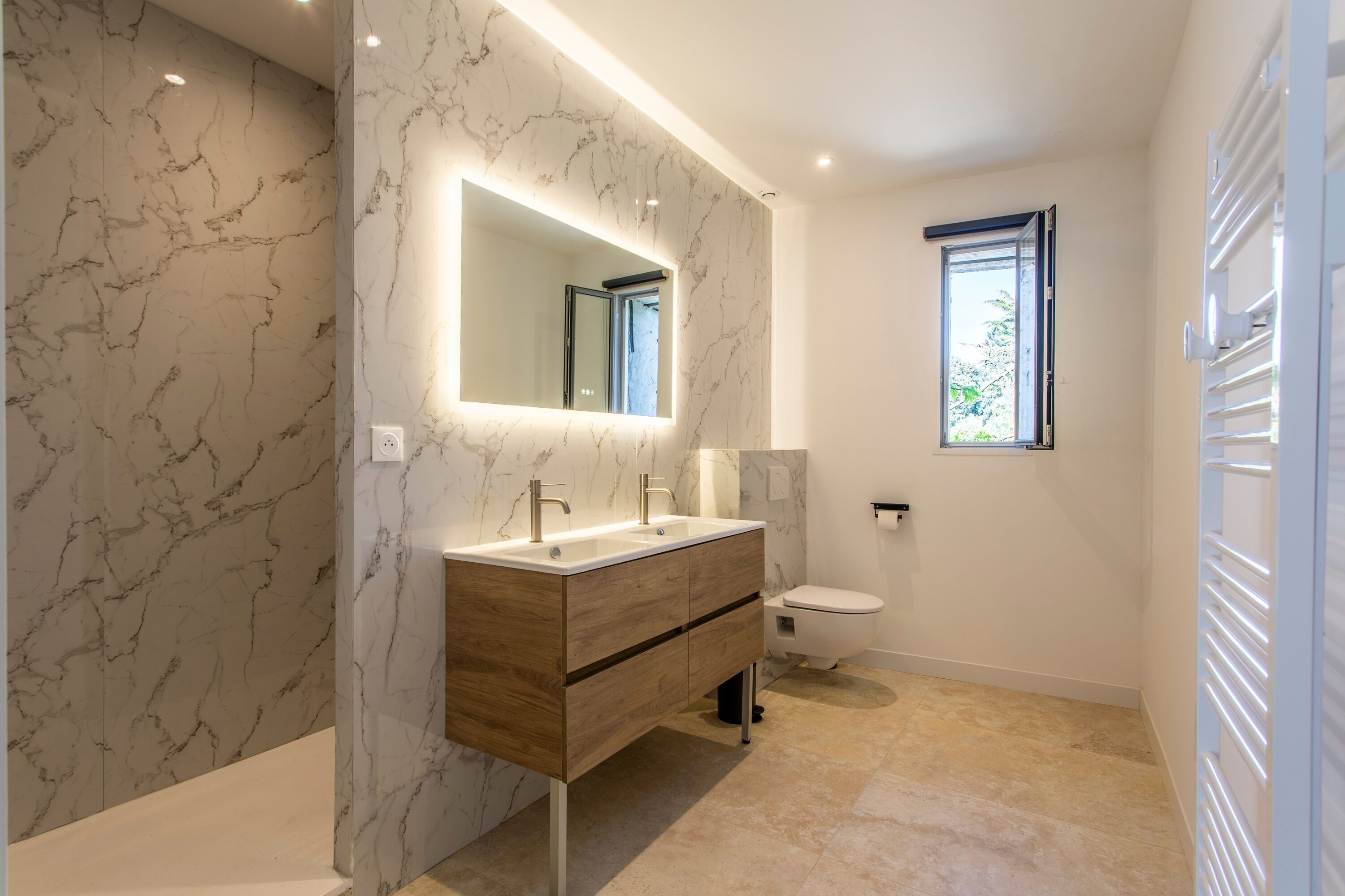 A modern bathroom with marble walls, a wooden vanity, a large mirror, and a toilet.