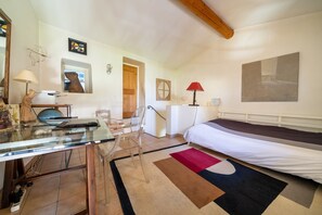 A bedroom with a bed, a desk with a computer, a chair, a window, and a door.