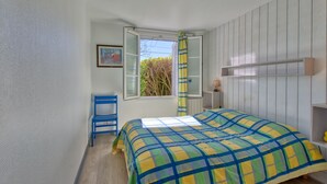 A bedroom with a bed, a chair, a window with curtains, a shelf, and a painting on the wall. - La Maison Orion - Oléron, à 1km de la plage (Dolus-d'Oléron)
