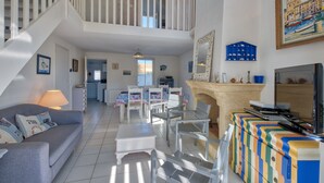 A spacious living area with a staircase, a dining table, and a television. - La Maison Orion - Oléron, à 1km de la plage (Dolus-d'Oléron)