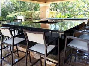 An outdoor bar area with a granite countertop, metal chairs, and a view of the surrounding greenery. - Cozy 1-bedroom apartment in amazing Miami with AC (Miami)