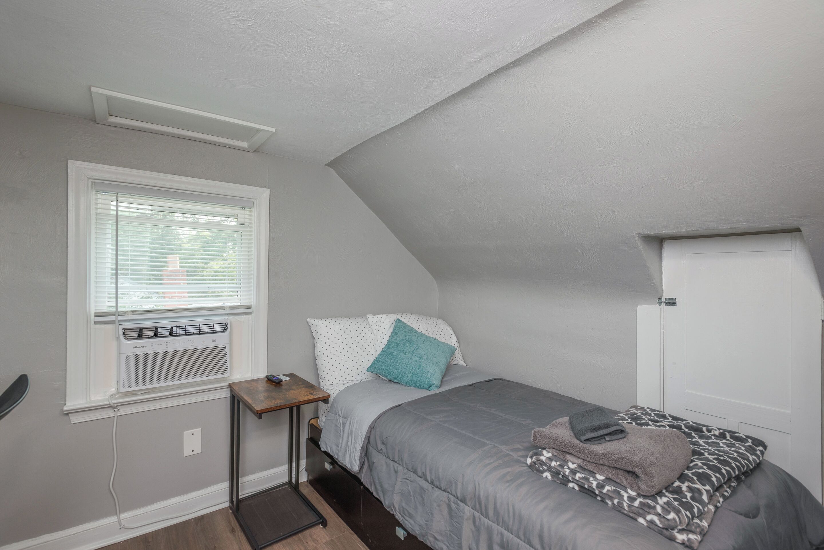 Een slaapkamer met een bed, een raam met zonwering, een verwarming en een deur.