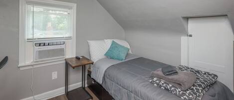 Een slaapkamer met een bed, een raam met zonwering, een verwarming en een deur.