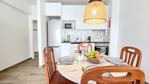 Een eethoek met een ronde tafel, vier houten stoelen, een mand vol fruit en een hanglamp.