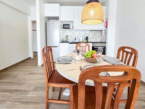 Ein Essbereich mit einem runden Tisch, vier Holzstühlen, einer Fruchtkorb und einer Pendelleuchte.