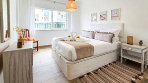 Een slaapkamer met een bed, nachtkastjes, een stoel, een raam en uitzicht op gebouwen.