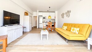 Een moderne woonkamer met een flatscreen televisie, een gele bank en een eethoek met stoelen en een tafel.