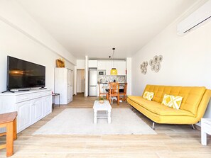 Ein modernes Wohnzimmer mit Flachbildfernseher, einem gelben Sofa und einem Essbereich mit Stühlen und Tisch.