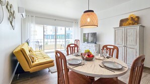 Een eetgedeelte met een ronde tafel, stoelen, een geel hoekbankje, een televisie en een kast.