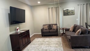 A living room with a flat-screen TV, dark brown leather sofas, a wooden cabinet, and a patterned rug. - New 3-bedroom house in beautiful Douglas with cool AC and warm heat (Douglas)