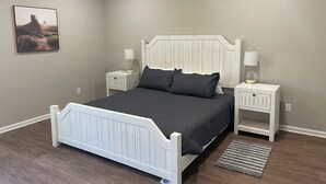 A bedroom with a white bed, two bedside tables, a nightstand, a rug, and a wall-mounted picture. - New 3-bedroom house in beautiful Douglas with cool AC and warm heat (Douglas)