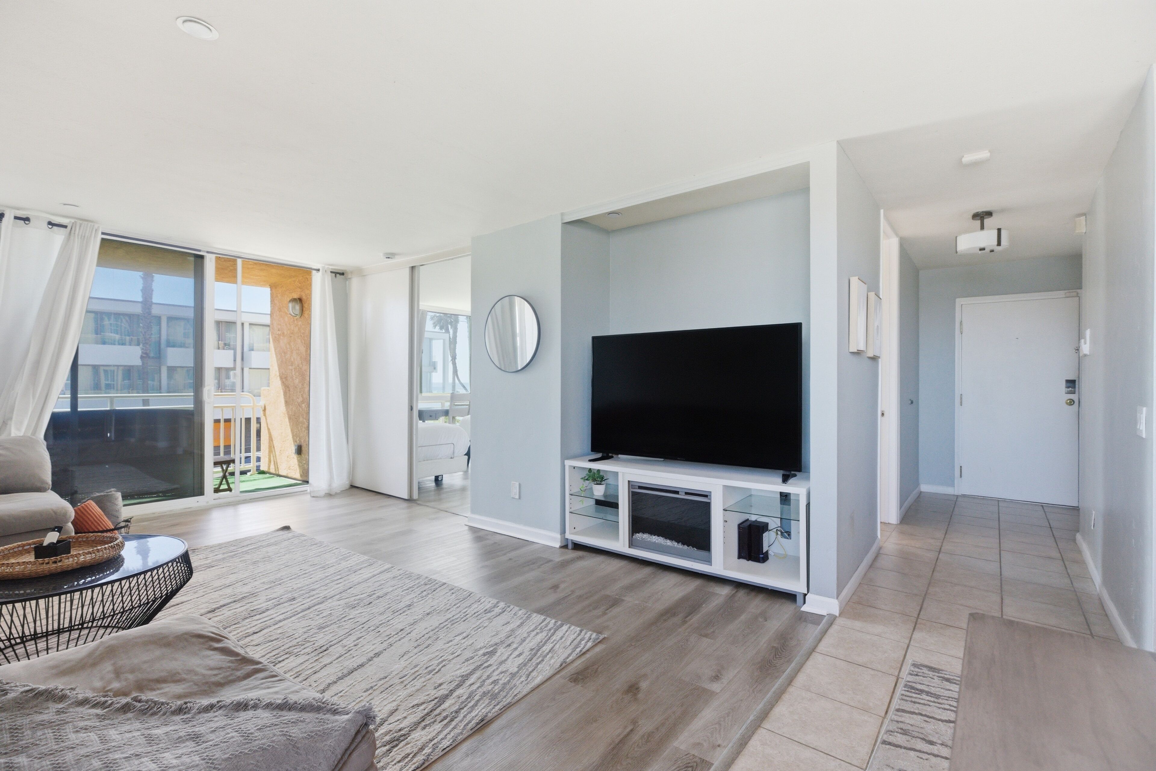 Een moderne woonkamer met een flatscreen televisie, een bank, een salontafel en een groot raam met gordijnen.