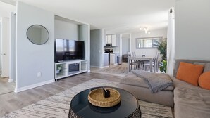 A modern living room with a flat-screen TV, a round coffee table, and a sofa. - Ocean View Oasis in Pacific Beach 2BR 2BA Balcony Pool  Monthly Stay (San Diego)
