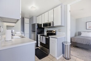 Eine kleine Küche mit weißen Schränken, einem Edelstahlkühlschrank, einer Mikrowelle und einem Backofen.
