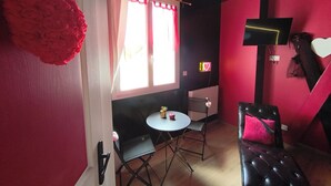 Una habitación con una mesa de comedor, sillas, un sofá, un televisor montado en la pared y una ventana con cortinas.
