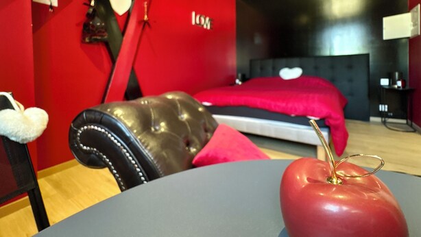 Un dormitorio moderno con una pared roja, una cama con cabecera roja y una butaca de cuero.