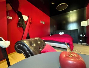 A modern bedroom with a red wall, a bed with a red headboard, and a leather chair.