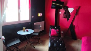 Una habitación con una pared negra y roja, un sillón de cuero negro, una mesita redonda y una ventana con cortinas.