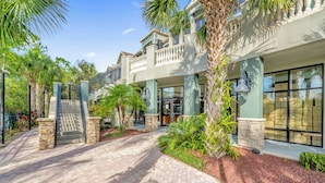 A multi-story hotel with a brick pathway leading to the entrance, surrounded by palm trees and greenery. - Upstay Pet-friendly Condo With Pool (Winter Garden)