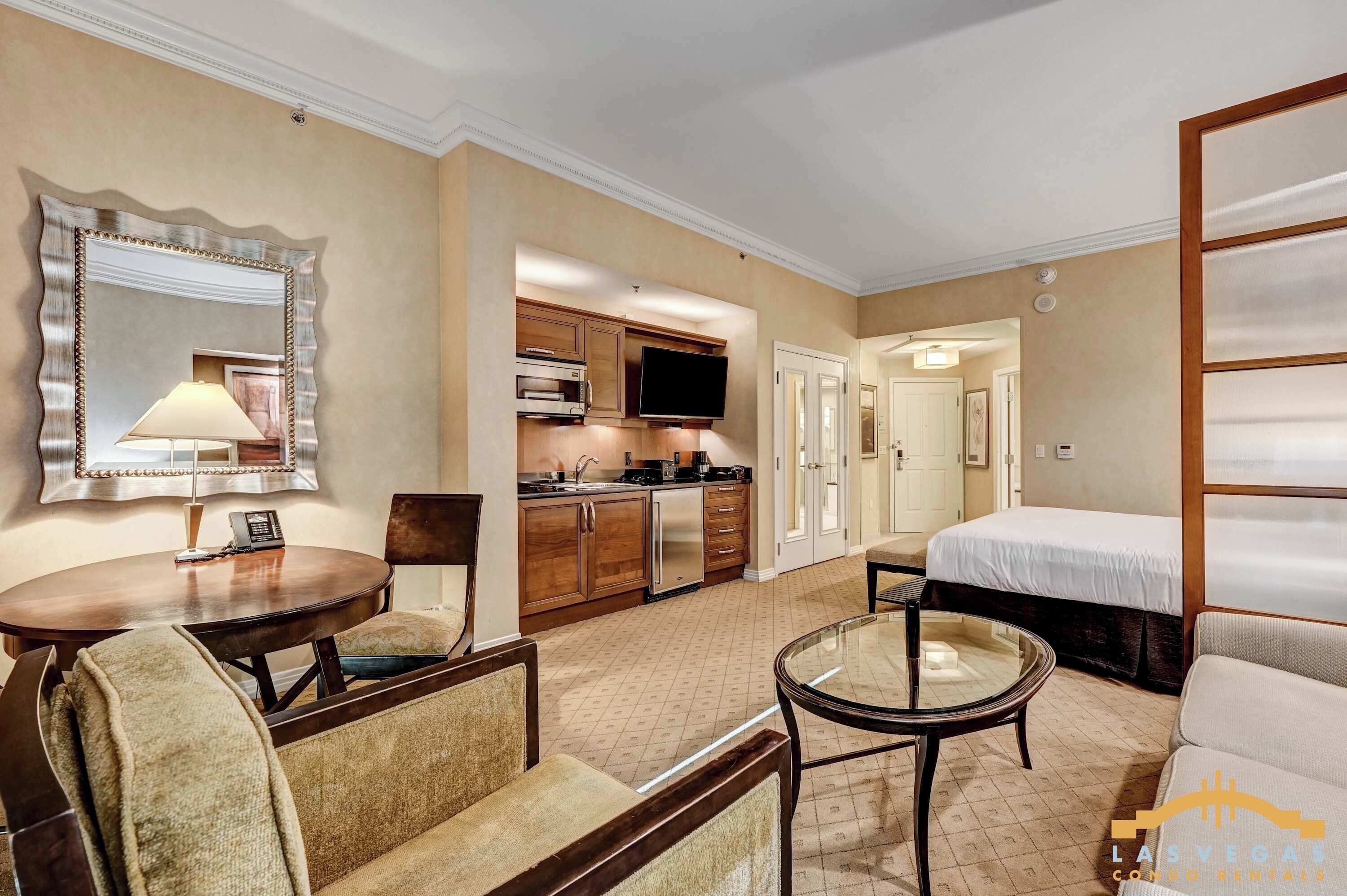 A hotel room with a dining area, kitchenette, and a bed.