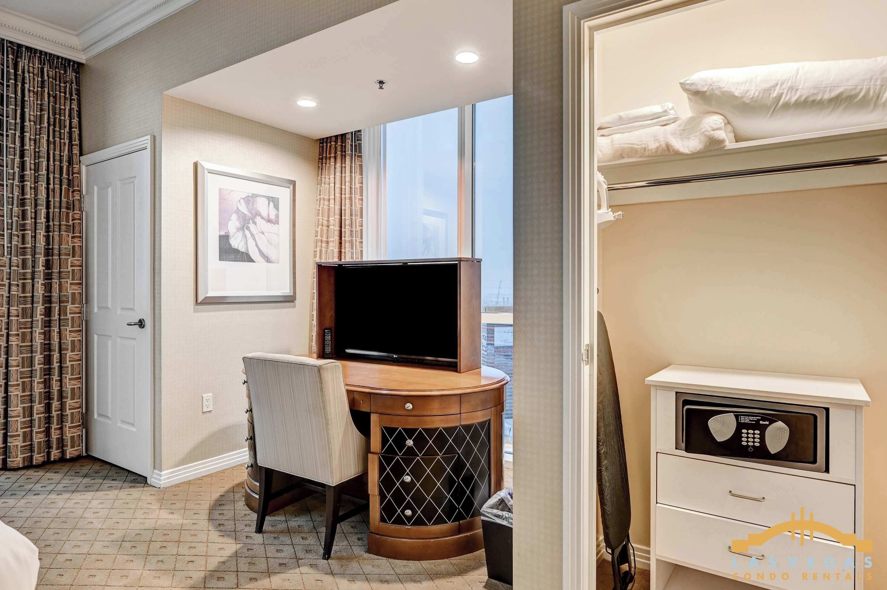 A hotel room with a bed, a desk with a TV, a chair, a microwave, and a window with curtains.