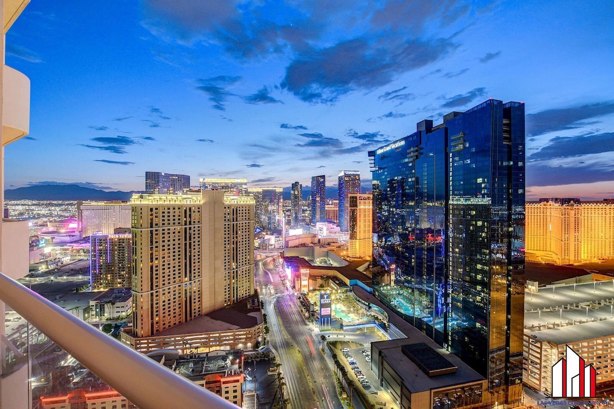Un hotel de gran altura con varios pisos, una fachada de vidrio destacada y vistas a un paisaje urbano con edificios e iluminaciones en las calles.