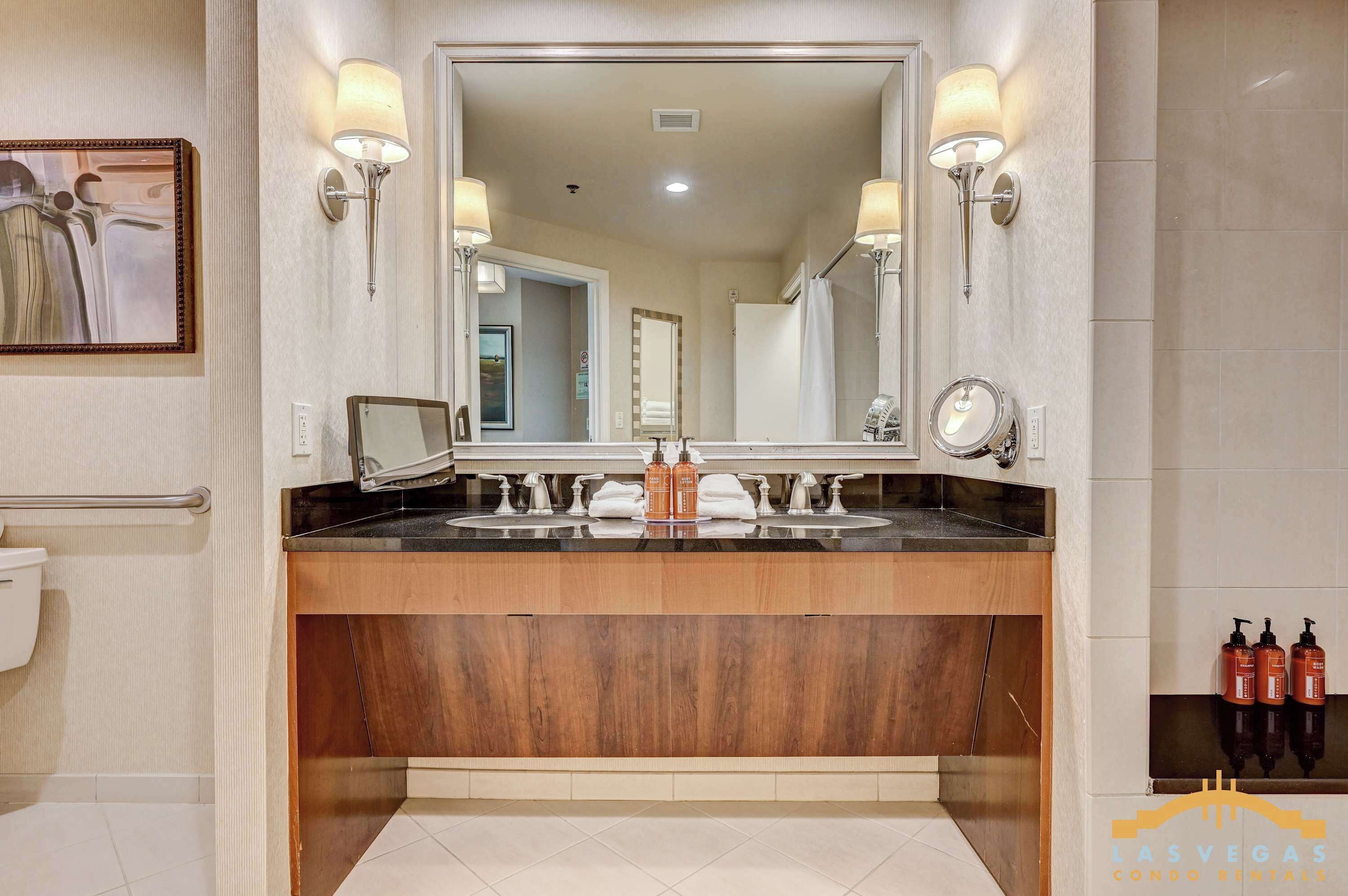 A bathroom with a large mirror, two sinks, and wall-mounted lights.