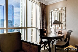A hotel room with a large window, a round table, a chair, a lamp, and a telephone. - MGM Signature (Las Vegas)